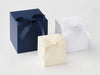 Three softbox gift boxes in blue, white, and ivory with ribbons on a light gray background